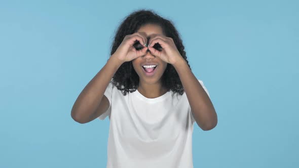 African Girl Searching with Handmade Binoculars Isolated on Blue Background