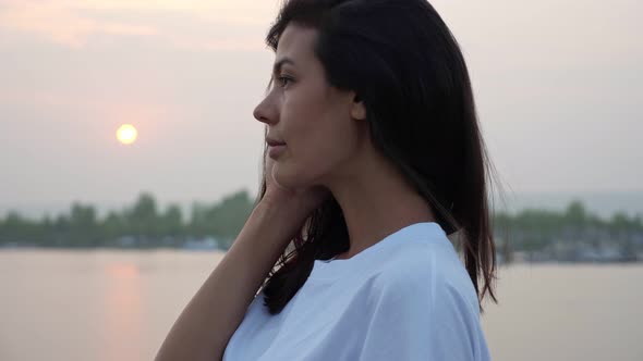 Pretty Woman Touches Cheek Against Tranquil River at Sunset
