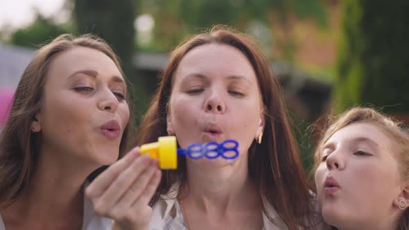Closeup Portrait of Joyful Pregnant Woman Blowing Soap Bubbles with Friends Sitting Outdoors on