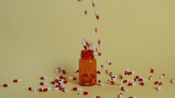 Slow motion wide shot as a handful of pills fall towards an open pill bottle. Some going in but most