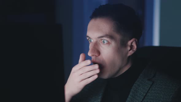 Afraid and Shocked Man Looking at Monitor Screen Takes Off Glasses and Cover His Mouth with His Hand