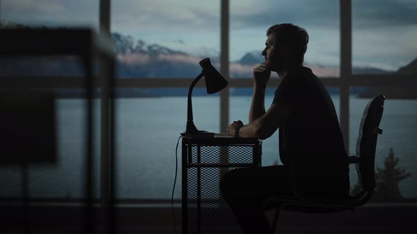 The Silhouette of a Thoughtful Man Sitting at a Table Against the Background of a Window with Oceans