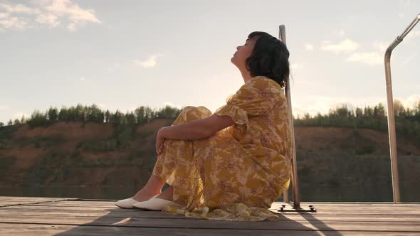 A young girl in a yellow dress sits on a wooden pier