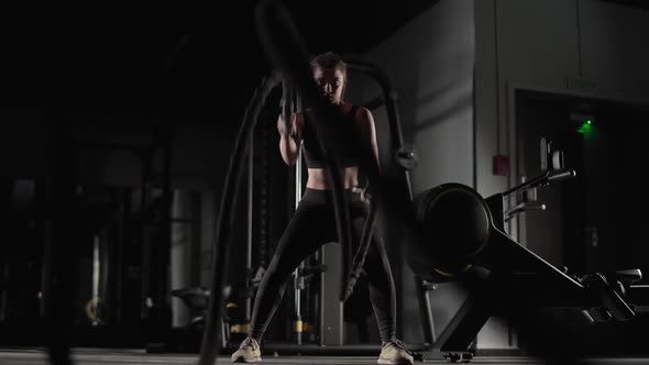 Handheld Athletic Female Performs Exercises with Battle Ropes Endurance Training in the Gym Slow