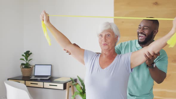 Video of happy caucasian senior woman exercising with african american male physiotherapist