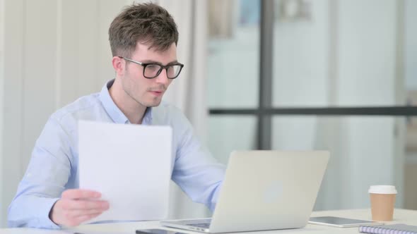 Man with Laptop Reading Documents in Office