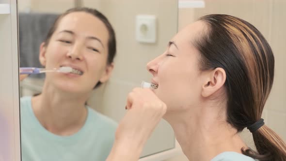 Woman with Braces Cleans Her Teeth with a Toothbrush Before Mirror Top View