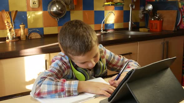 A Cute Boy of 7 Years Old Sits in the Kitchen at the Table Looks at the Desktop Monitor