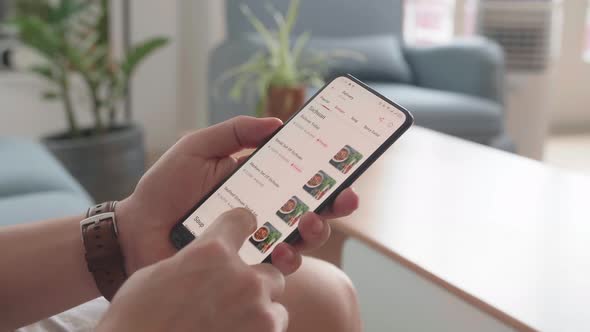 Close Up Of Man Hand Holding Smartphone And Orders Food In Online Store