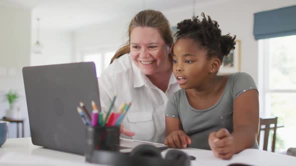 Happy caucasian woman and her african american daughter doing homework together