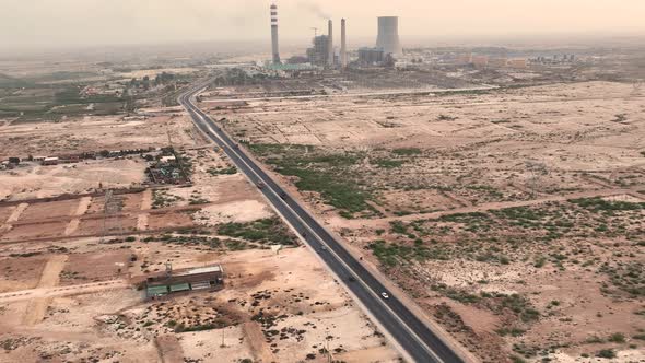 Cinematic aerial shot of silver car driving on country road in desert and big chimneys in distant ba