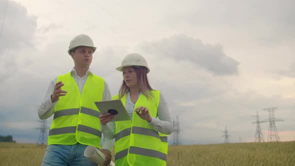 Power Lines Man and Woman Engineers with a Tablet in Their Hands Check the Progress of the