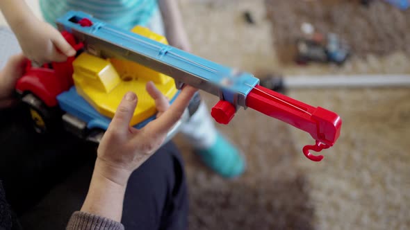 the Hands of a Child and the Hands of an Adult are Playing a Big Colored Car with a Crane