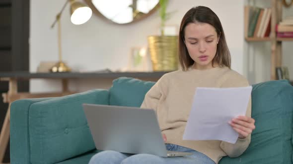 Young Woman with Documents Working on Laptop on Sofa