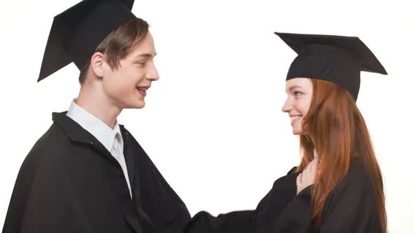 Happy Caucasian Graduate Boy and Girl in Black Robes and Square Academical Caps Cheering Each Other