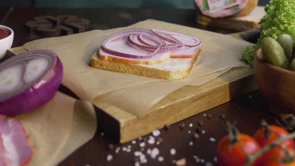 The Cook Adds Sliced Tomato To the Sandwich with Ham and Vegetables on the Wooden Board in the Beam