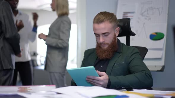 Portrait of Focused Concentrated Caucasian Bearded Man Surfing Internet on Tablet Sitting at Table