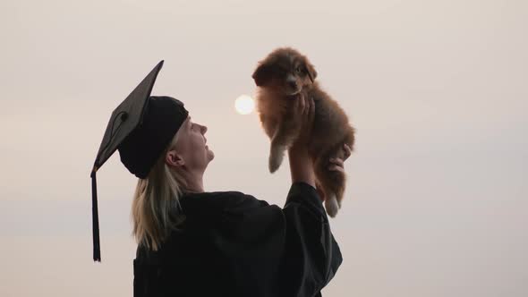 A Woman in a Graduate Costume Holds a Cute Puppy in Her Arm