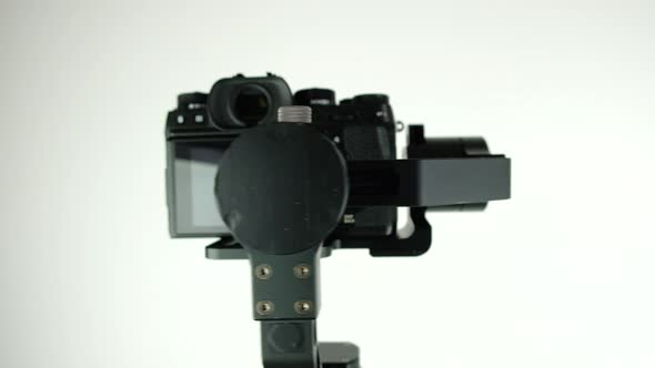 Gimbal with digital camera rotates on white background.