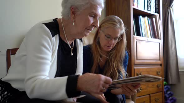 Closeup of elderly woman and blonde mature woman looking at photos out of a photo album.