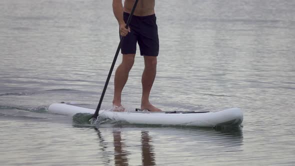 A man paddles his SUP stand-up paddleboard in a lake.