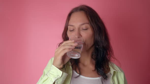 Woman Drinking Water From a Glass on a Pink Background