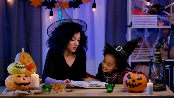 Little African American Girl in Festive Costume and Witch Hat Read Book