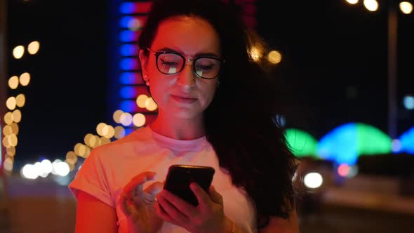 Pretty Woman Stands on the Street in a White T-shirt and Glasses, Makes Online Payments By Credit