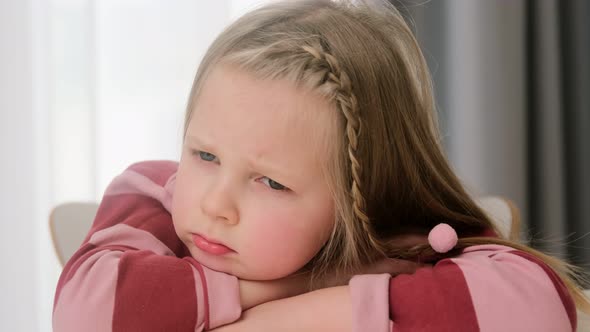 Sad upset offended child little girl sits at a desk. Kid punished, lonely problems