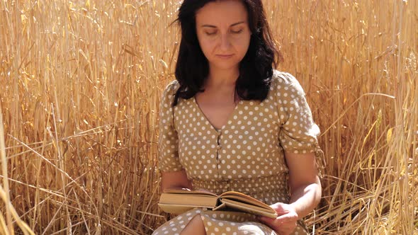 A Girl Reads a Book, Sitting in Nature Among a Field of Ripe Wheat. Sunny Summer Day. Lifestyle