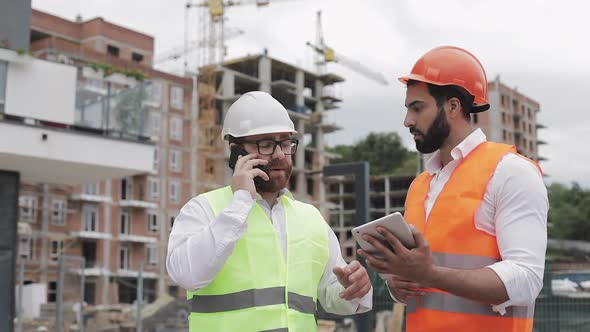 Engineer Speaks on Mobile Phone on Construction Site and Checks the Work of the Worker