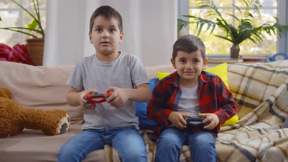 Cute Preschool Boys Playing Video Game Holding Joysticks Sitting on Couch at Home