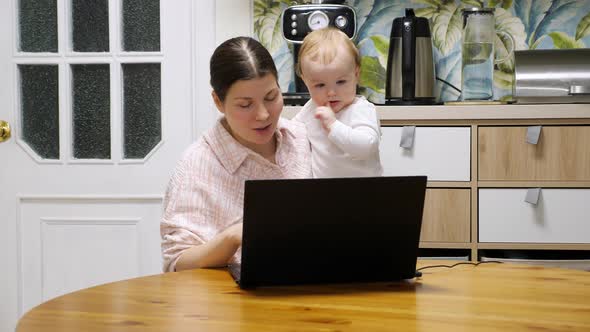 Woman with baby are talking on video link, her eldest daughter runs up and joins