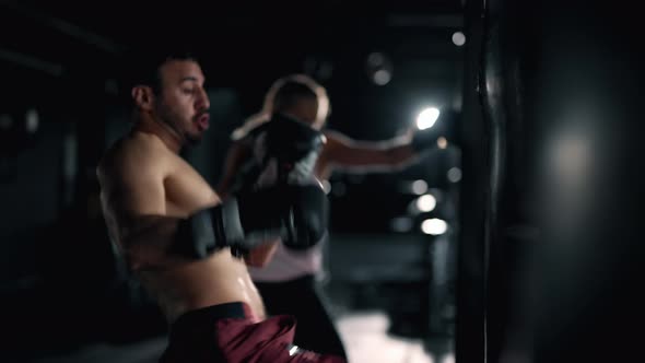 A Muscular Man and Woman are Hits Punching Bag in the Gym