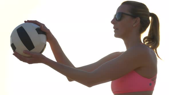 Women players play beach volleyball and a player serves the ball.