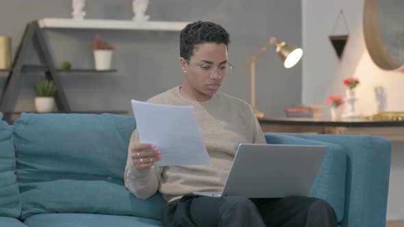 African Woman with Laptop Working on Documents on Sofa