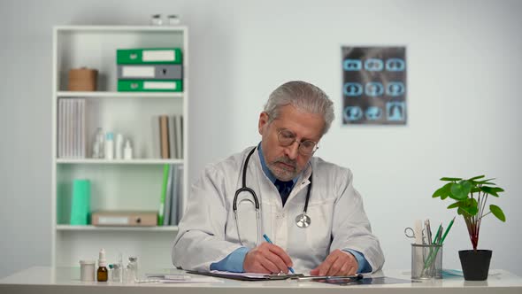 Aged Male Doctor Fills in the Patient's Medical History in a Black Folder
