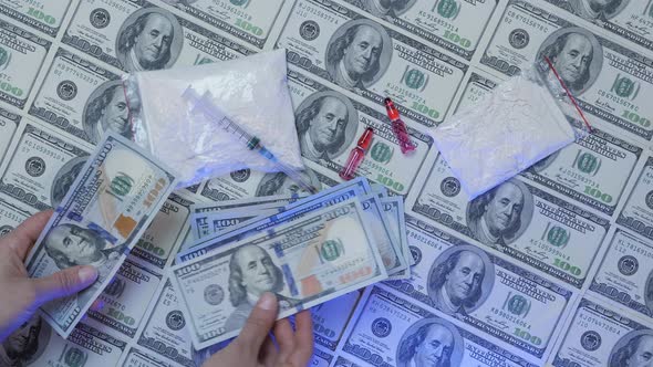 Hand counting money against drugs, syringe and dollars background