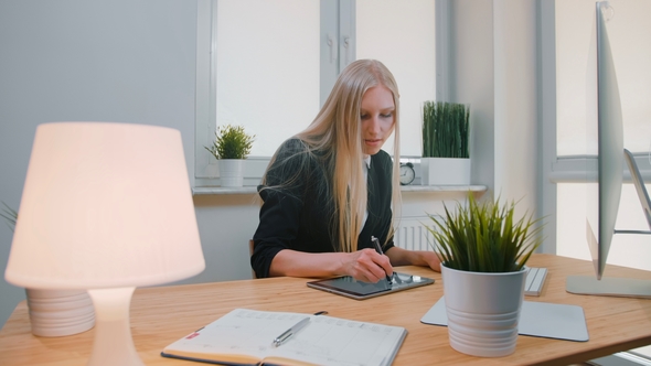 Business Women Working on Tablet in Office. Attractive Blond Female with Long Hair in Elegant Suit