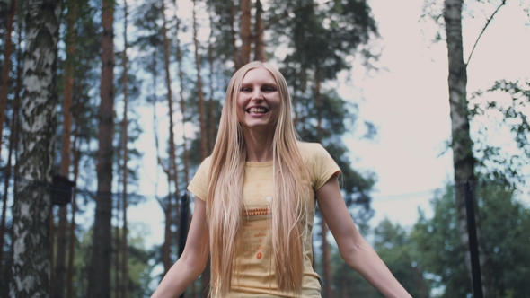 Happy Female Jumping on Trampoline. Beautiful Young Blond Barefoot Woman in Light Summer Shirt and