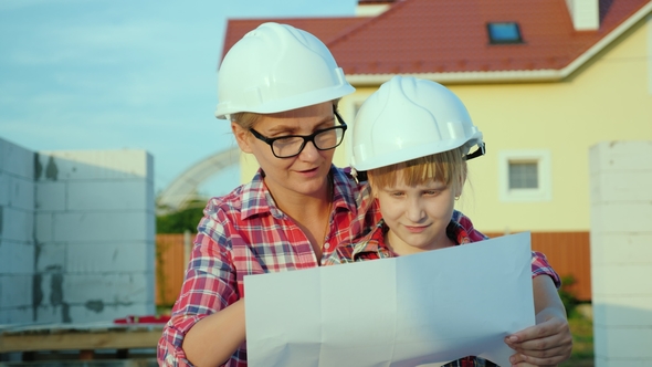 A Woman in a Helmet with a Child Looks at the Drawing of the House