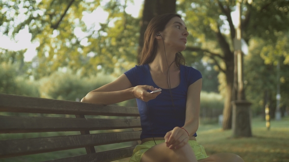 Pretty Woman Enjoying Music on Park Bench