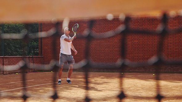 Young Attractive Man Playing Tennis on Orange Clay Tennis Court