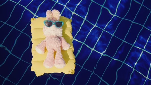 A Pink Bunny in Sunglasses Is Floating on an Inflatable Mattress in the Pool