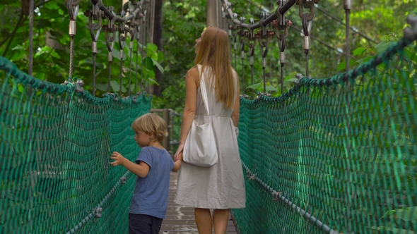 Young Woman and Her Son Walking on the Hanging Suspension Bridge in the Eco Park