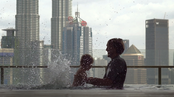 Father and Son Having Fun in a Rooftop Pool with a View on Skyscrapers