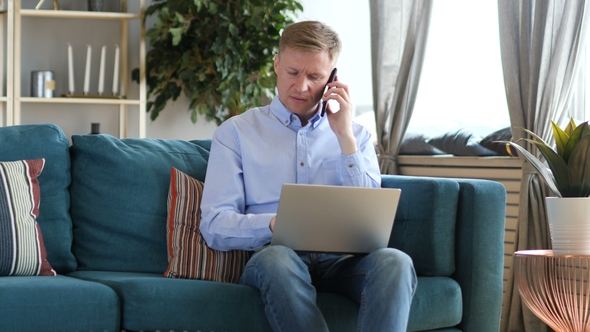 Middle Aged Man Talking on Phone and Working on Laptop