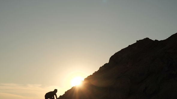 A Man Climbs the Slope of the Mountain at Sunset