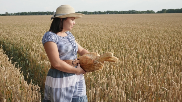 A Young Woman Is Carrying Bread in a Basket on a Wheat Field