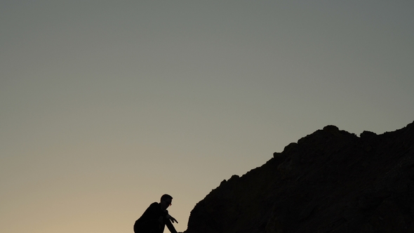 Silhouette of a Businessman with Difficulty Climbs Uphill and Triumphantly Raises His Hands Upwards